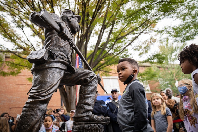 A child stands in front of a statue honoring Black soldiers.