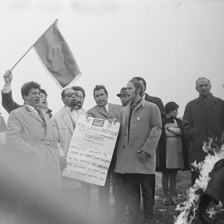 The inaugural World Romani Congress in 1971 near London was a meeting of minds bent upon defining a nation whose disparate members have been scattered around the world. The 23 delegates chose the word “Roma” as the official name. They adopted, as the elements of the flag, a red chakra, the sixteen-spoke wheel of India, set on a field of green and blue. And they chose “Gelem, Gelem,” a song of suffering and the endless road, as the national anthem. Photo credit: © Eva Davidová A group celebrating and holding a flag