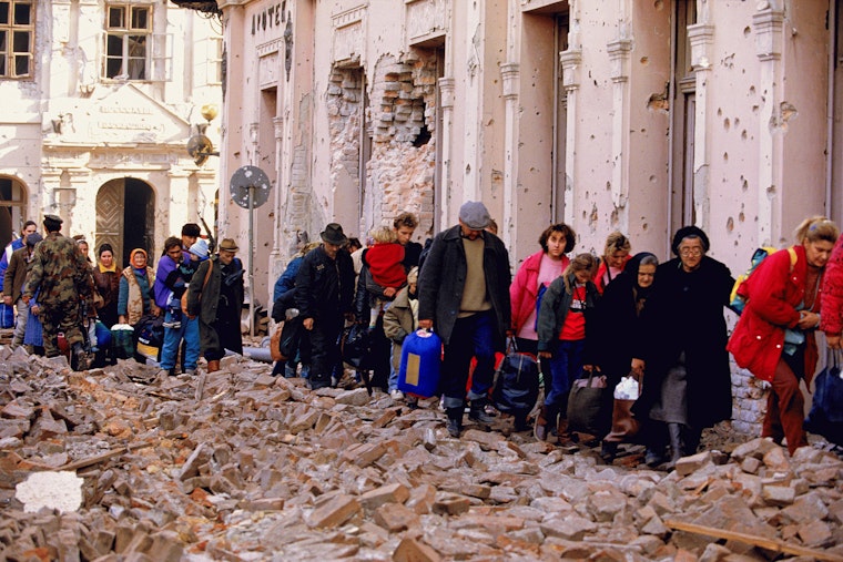 A line of Croatians walk through rubble