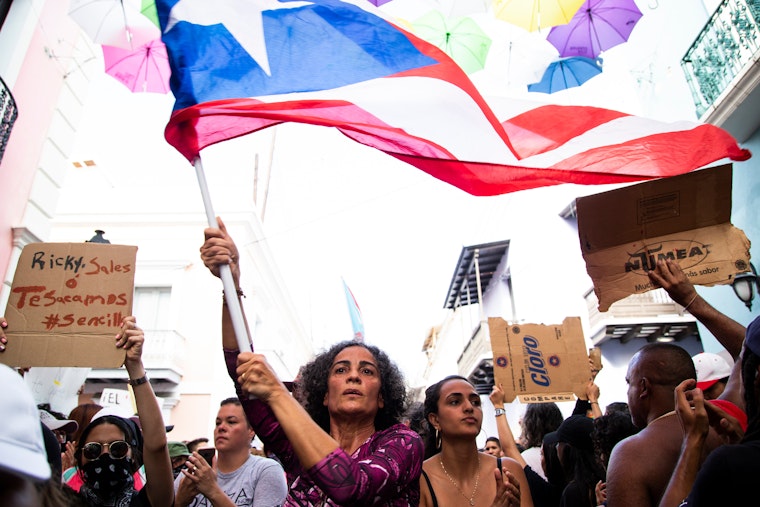 Mujer alzando la bandera de Puerto Rico junta a otros manifestantes