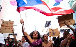 Mujer alzando la bandera de Puerto Rico junta a otros manifestantes