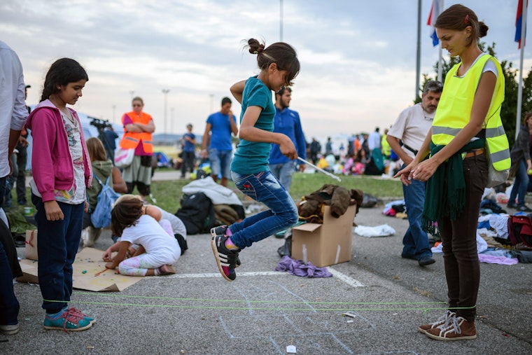 A volunteer plays with children as migrants wait to be taken from the Slovenian border to a registration center in Bregana, Croatia, in September 2015. Photo credit: © Jure Makovec/Getty Girl jumping in the air