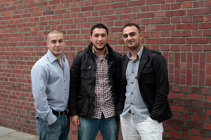 Three men posing for picture in front of brick wall