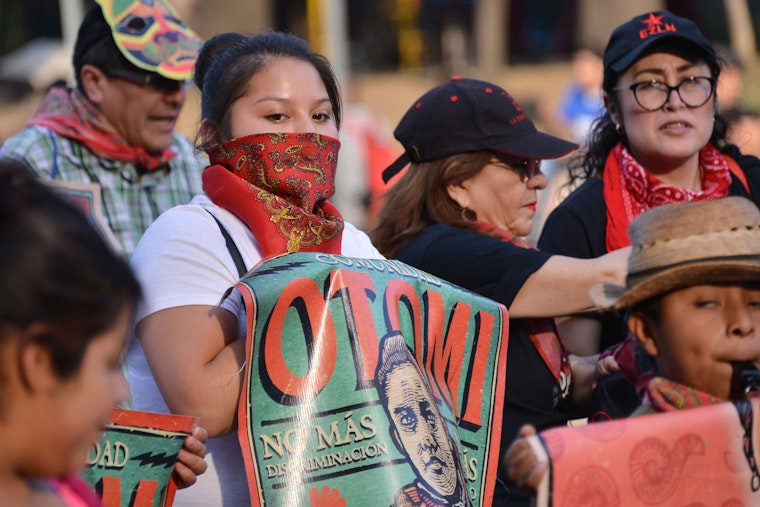 Protesters gather and a woman holds a poster.