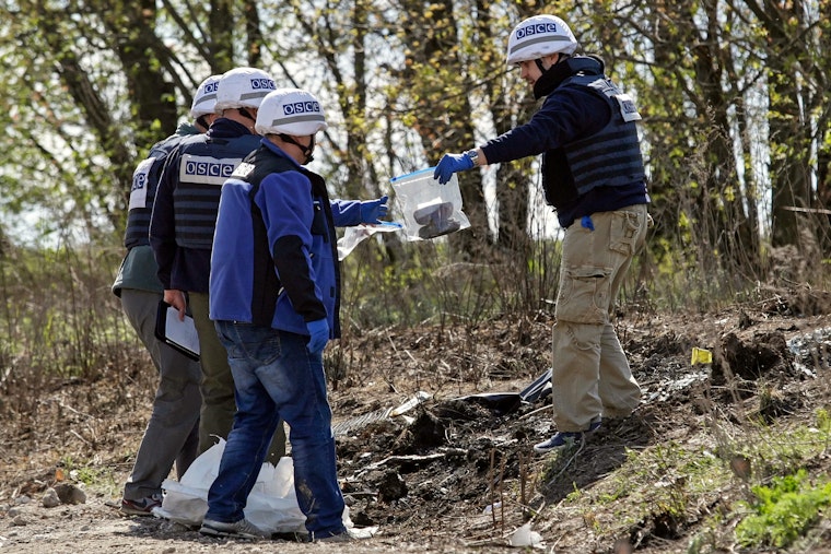 Three people in safety vests and helmets collect evidence